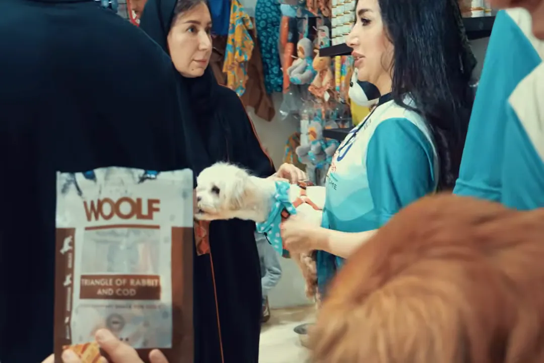 A volunteer handing a small dog to a visitor at a Liqa adoption day in Jeddah
